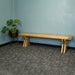 An overall view of the Arpege Oak Cross Leg 2m Bench Seat. There is a free standing potted plant next to it.