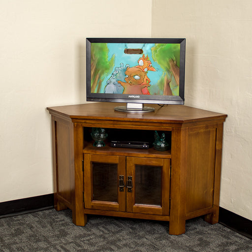 The front of the Montreal Pine Corner Entertainment Unit with a TV on top. There is a DVD player and two blue glass ornaments on the shelf.