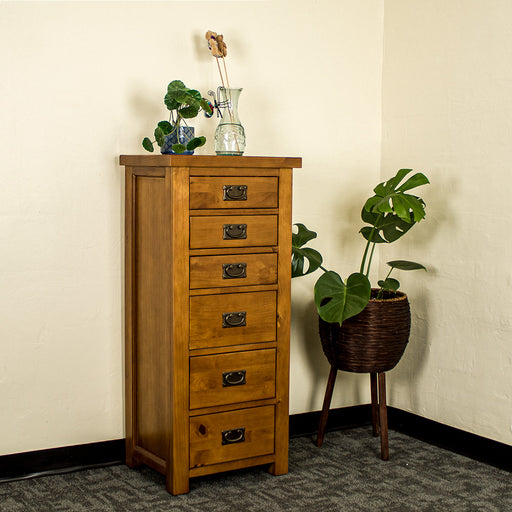 The front of the New Quebec 6 Drawer Lingerie Chest. There is a potted plant on top and a blue glass vase. There is a free standing potted plant next to it.