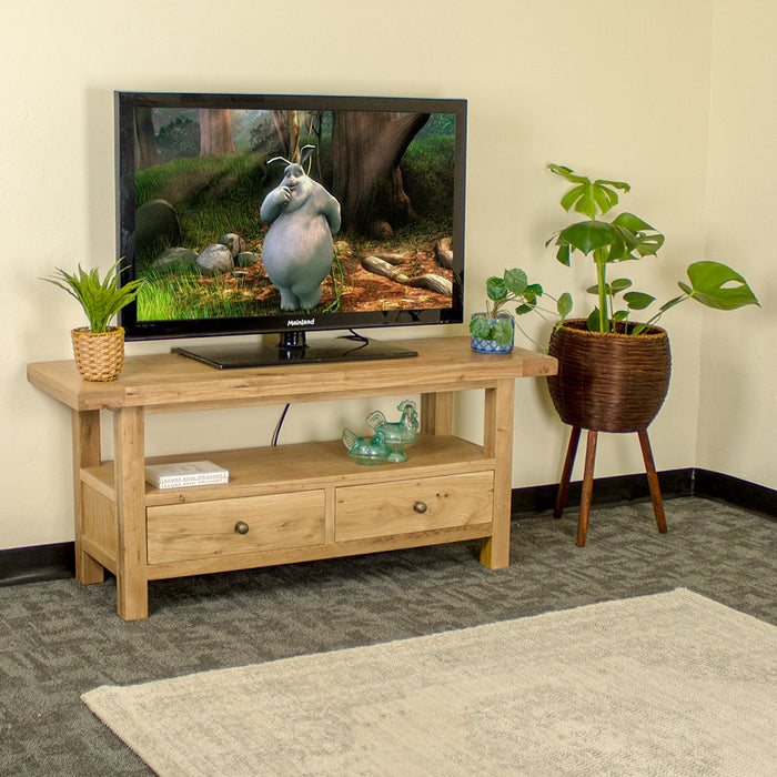 The front of the Farmhouse Entertainment Unit. There is a large TV on top, with two small potted plants on either side. There is a free standing potted plant next to it. There is a rug in front of the TV cabinet. There are two DVDs and two blue glass ornaments on the shelf below the TV.