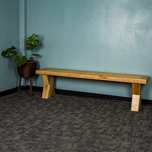 The front of the Maximus Oak Cross Leg Bench Seat (1.9m). There is a free standing potted plant next to it.