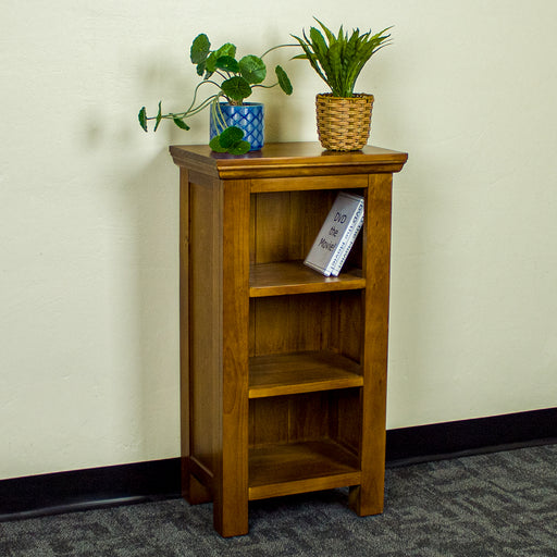 The front of the Montreal Compact Pine Bookcase, with two potted plants on top. There are two DVD cases on the top shelf.
