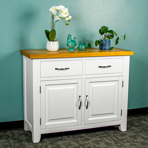The front of the Felixstowe Small Pine Buffet (White). There are two potted plants with two blue glass ornaments in between on top of the sideboard.