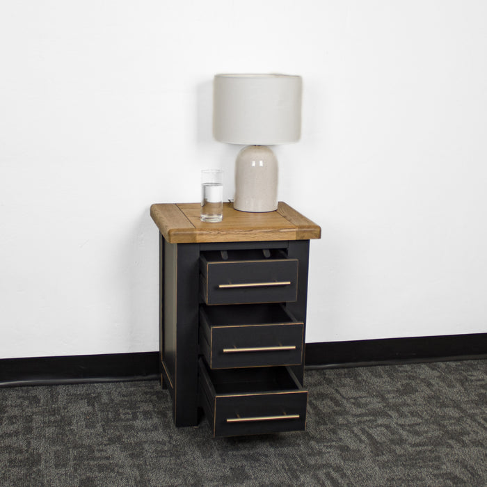 The front of the Cascais 3 Drawer Black Bedside Table with its drawers open. There is a glass of water and a lamp on top.