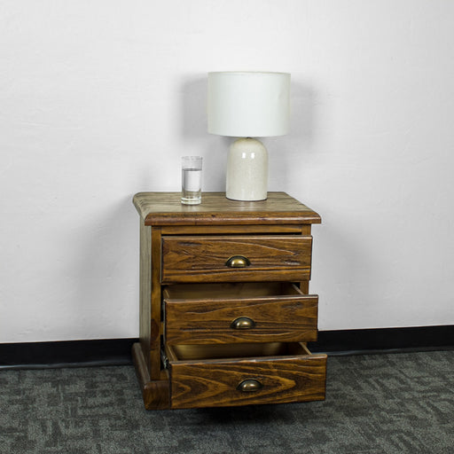 The front of the Heid Large 3 Drawer Pine Bedside with its drawers open. There is a lamp and a glass of water on top.