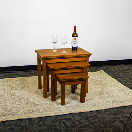 The Montreal 3 Piece Pine Nesting Tables, out from underneath each other. There are two wine glasses and a bottle of wine on the top table.