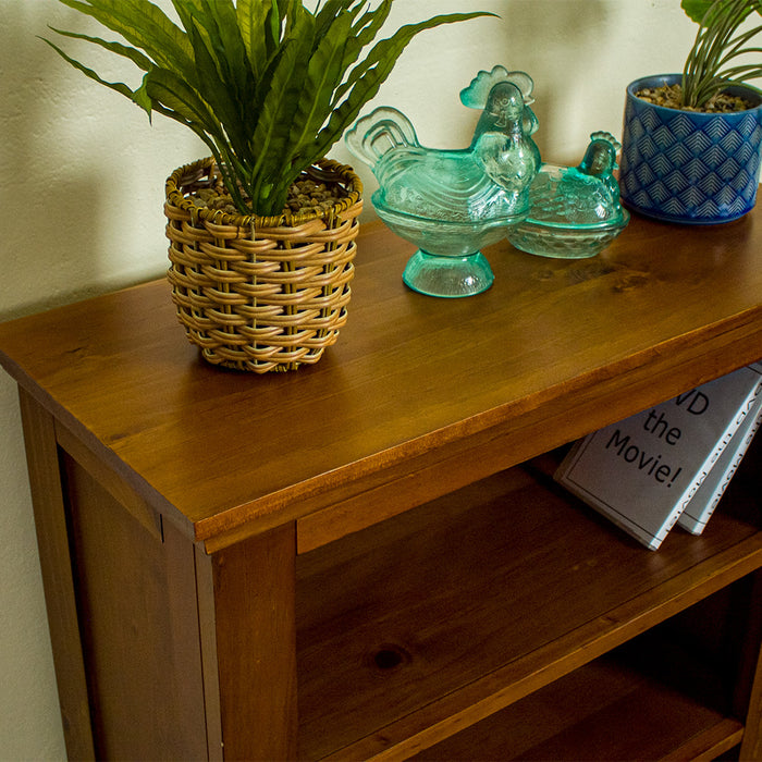 The top of the Montreal Low Pine Bookcase, showing the wood grain and colour. There are two potted plants on top with two blue glass ornaments in the shape of chickens inbetween.