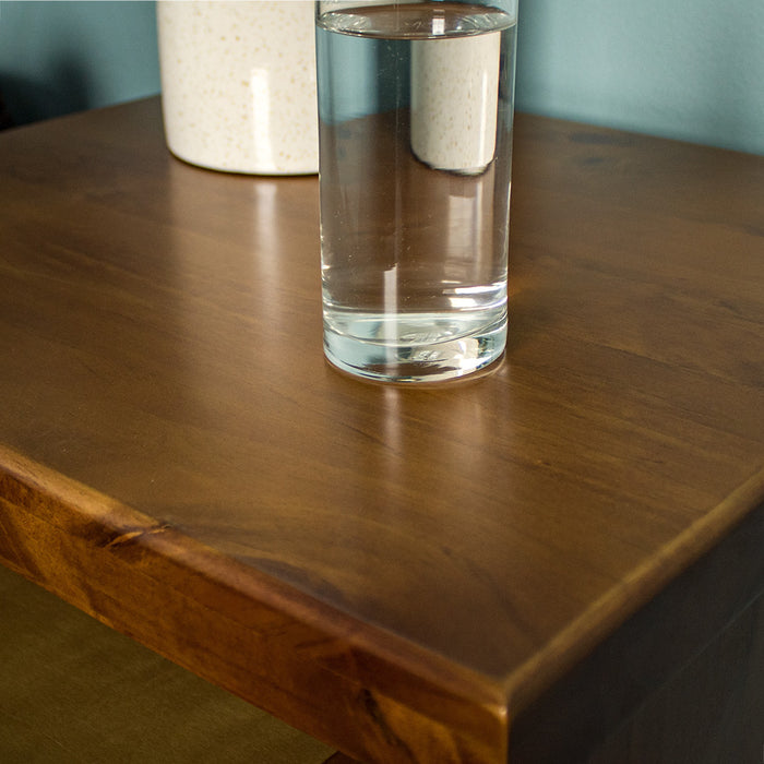 A close up of the top of the Jamaica Bedside Cabinet, showing the wood grain and colour. There is a glass of water on top.