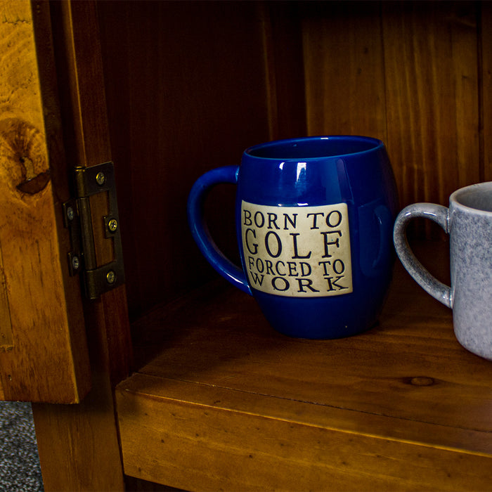 A closer view of the hinge on the door of the Montreal Compact Pine Buffet. There is a coffee mug in view that reads "Born to Golf forced to Work".