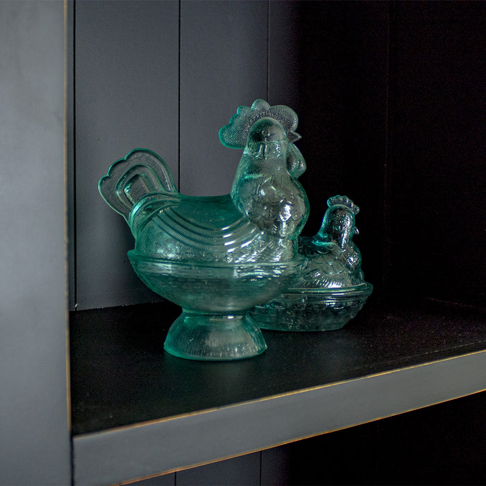 A close up of the shelf on the Cascais Tall Black Bookcase. There are two blue glass ornaments in the shape of chickens.