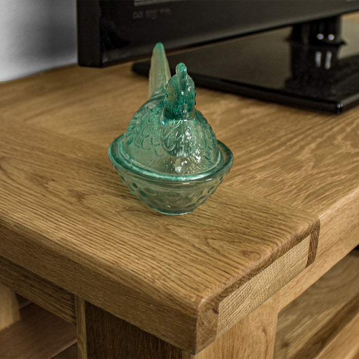 A close up of the top of the Camden 2 Drawer White Oak Entertainment Unit, showing the wood grain and colour. There is a blue glass ornament in the shape of a chicken on top.