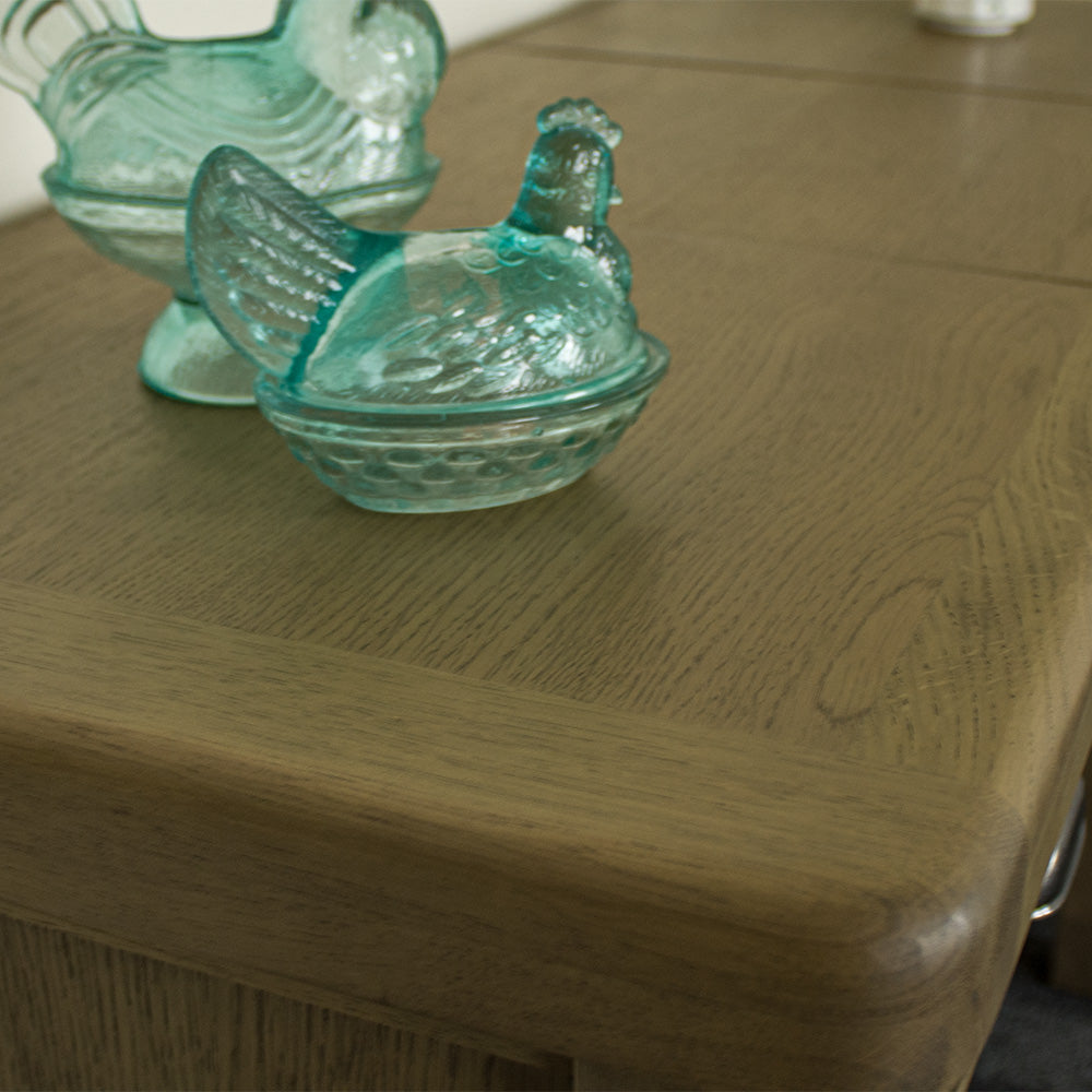 A close up of the top of the Houston Oak Dressing Table With Mirror, showing the wood grain and colour. There are two blue glass ornaments in the shape of chickens on top.